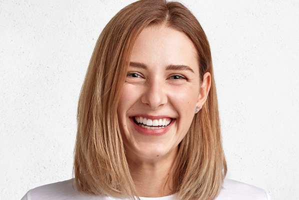 Headshot of smiling female dental implant patient with shoulder-length strawberry blonde hair
